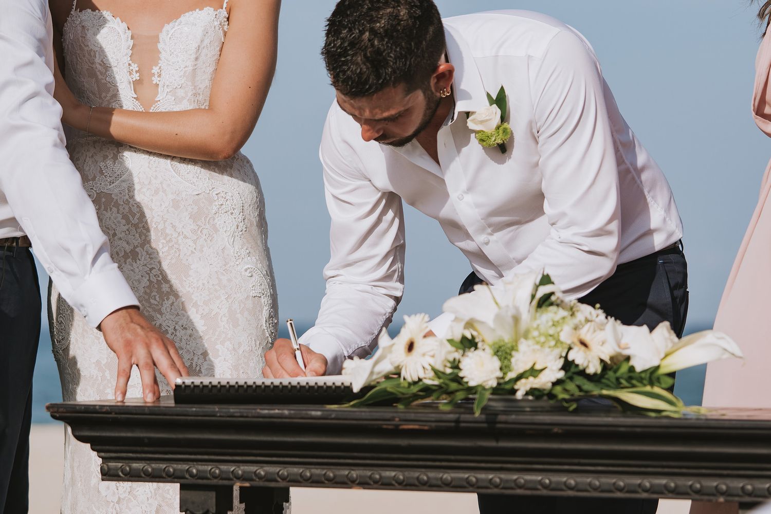 Couple signing marriage certificate on dark table with white floral arrangement.