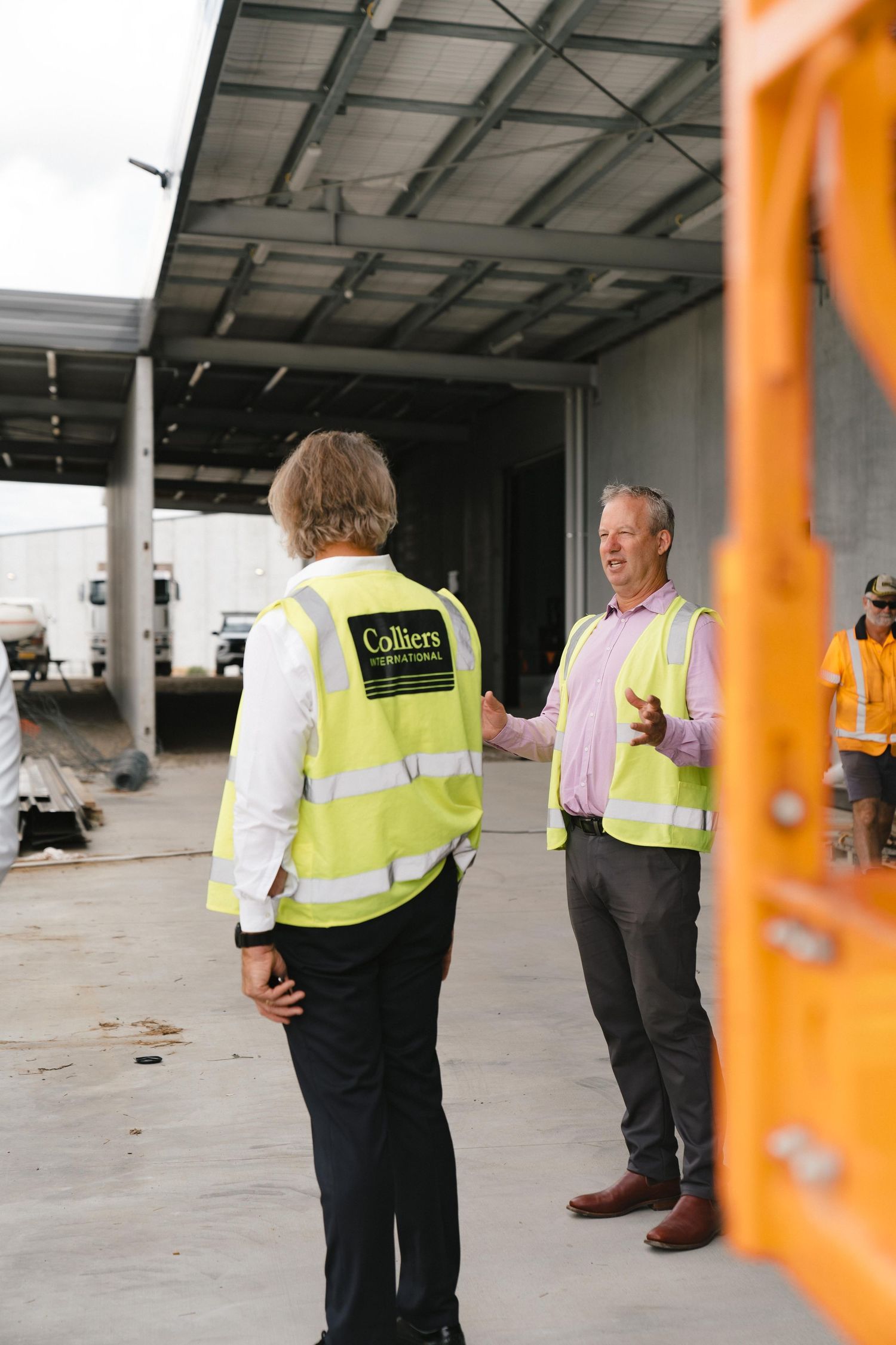 Construction site meeting between two people wearing high visibility vests in an industrial setting.
