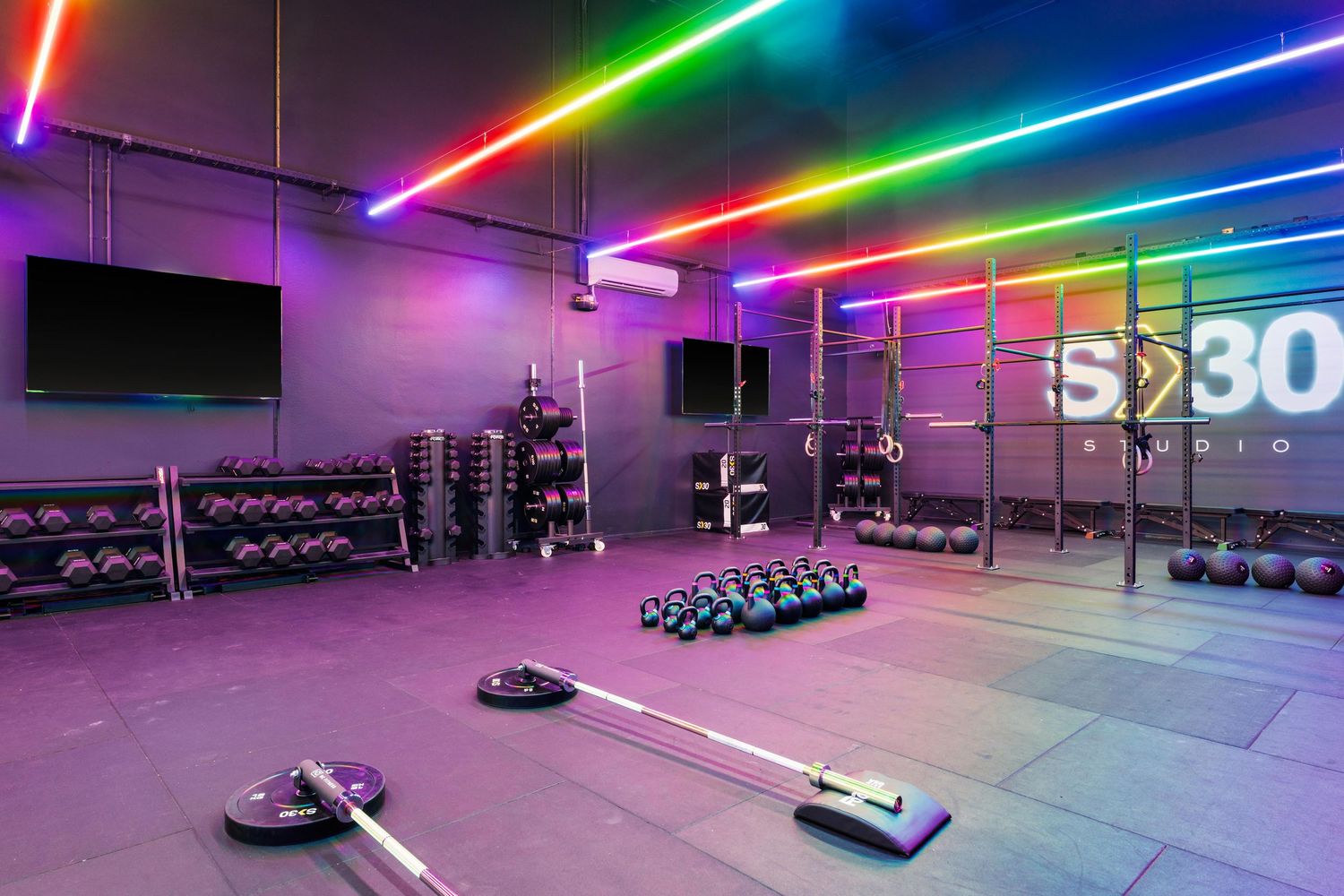 Fitness studio with free weights and equipment illuminated by vibrant rainbow LED lighting on ceiling and walls.