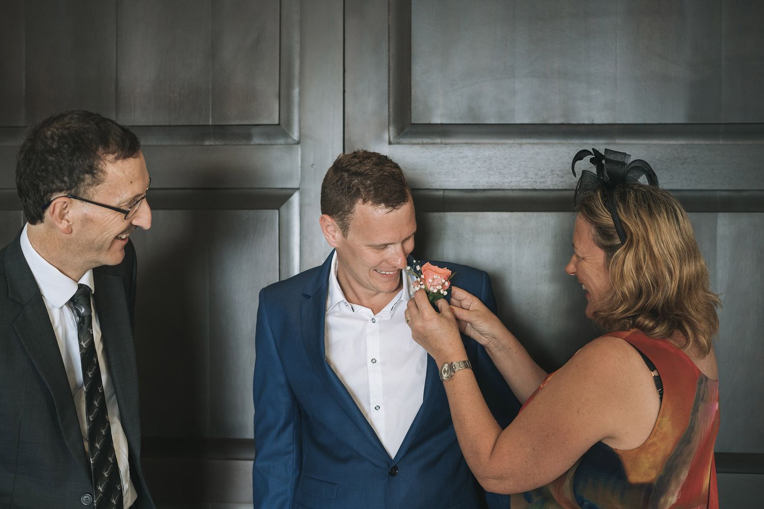 Boutonniere being pinned on groom's lapel during wedding preparation.