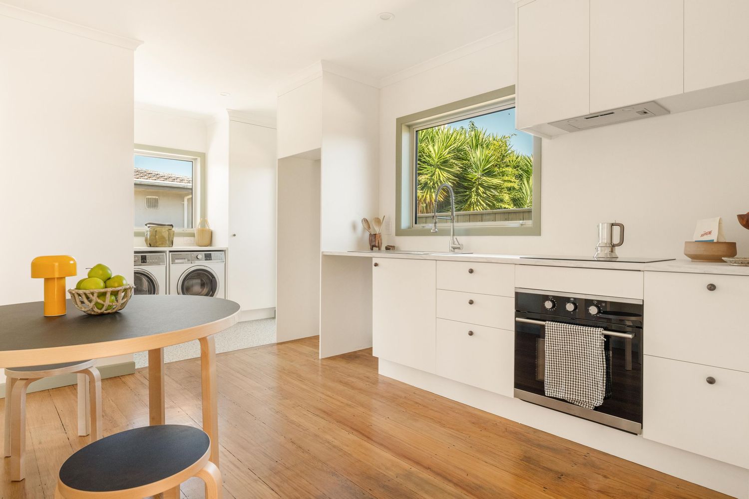 Modern white kitchen with hardwood floors and a round dining table near large window.
