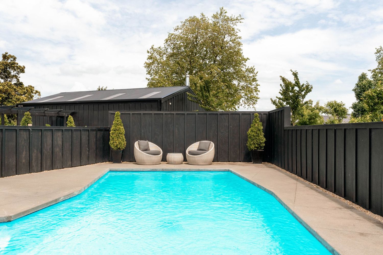 Large outdoor swimming pool with dark privacy fence and decorative garden features.
