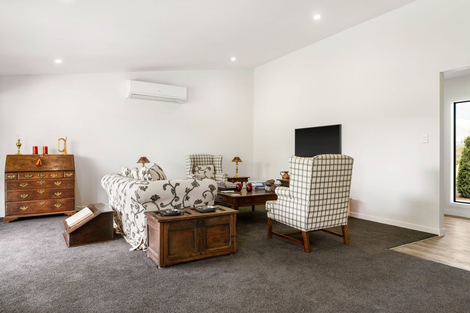 Minimalist bedroom interior with grey carpet, white walls and recessed lighting showcasing elegant wood furniture.