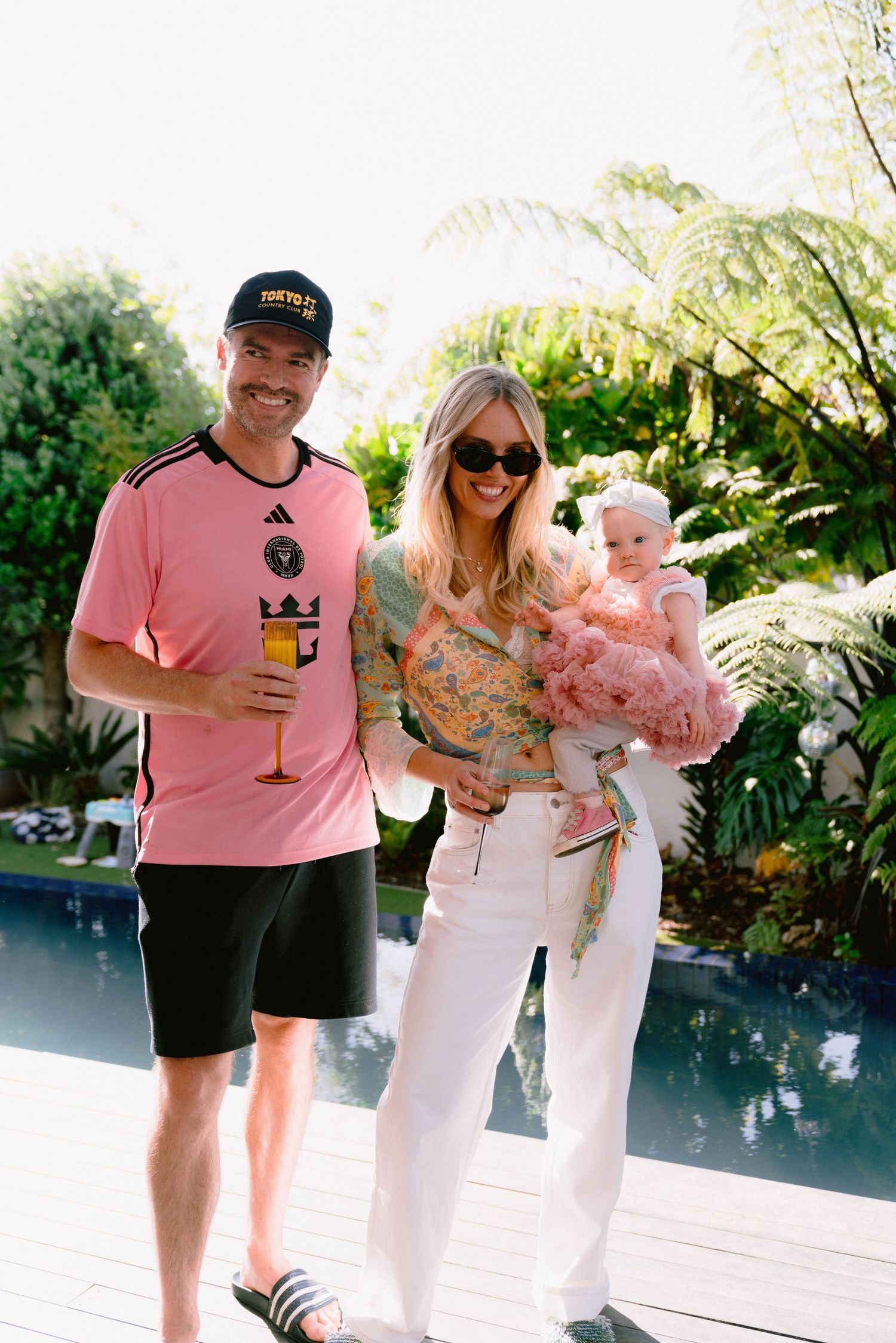 Group of people enjoying a poolside gathering with someone wearing a pink shirt and baseball cap.
