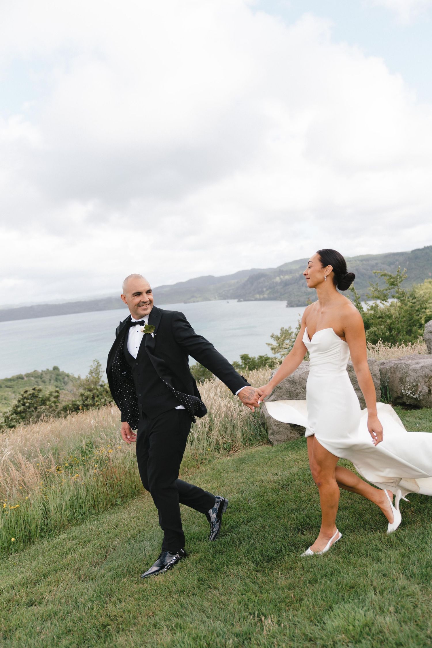 Couple playfully dancing on a grassy hillside overlooking the ocean.