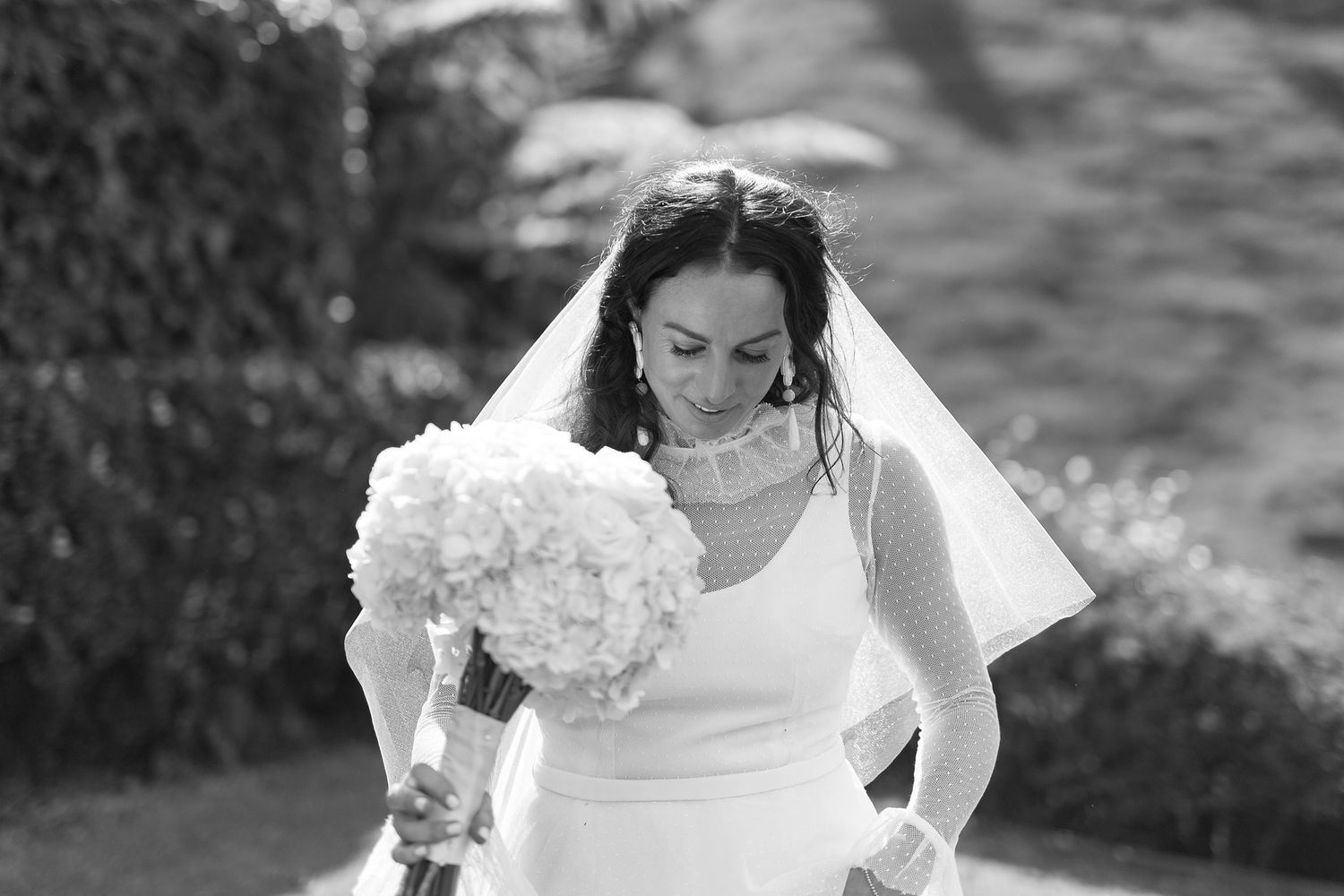 A bride in an elegant white gown descends stone stairs while looking down and holding her dress.