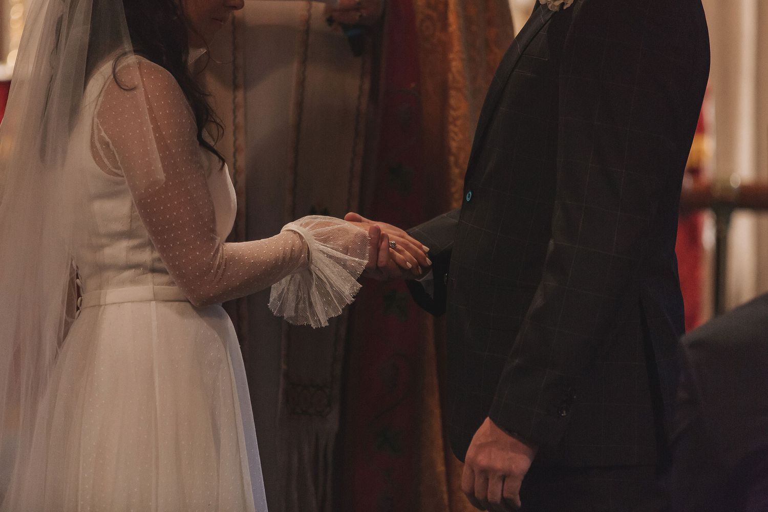 Two people join hands during a wedding ceremony with the bride wearing a white dress with flowing veil.
