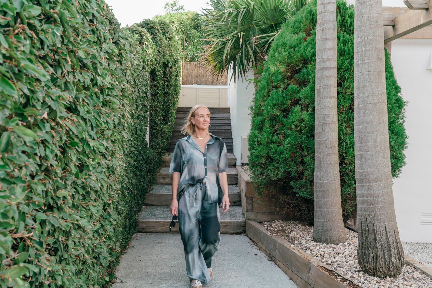 Garden pathway between tall hedges with palm trees and stone steps.