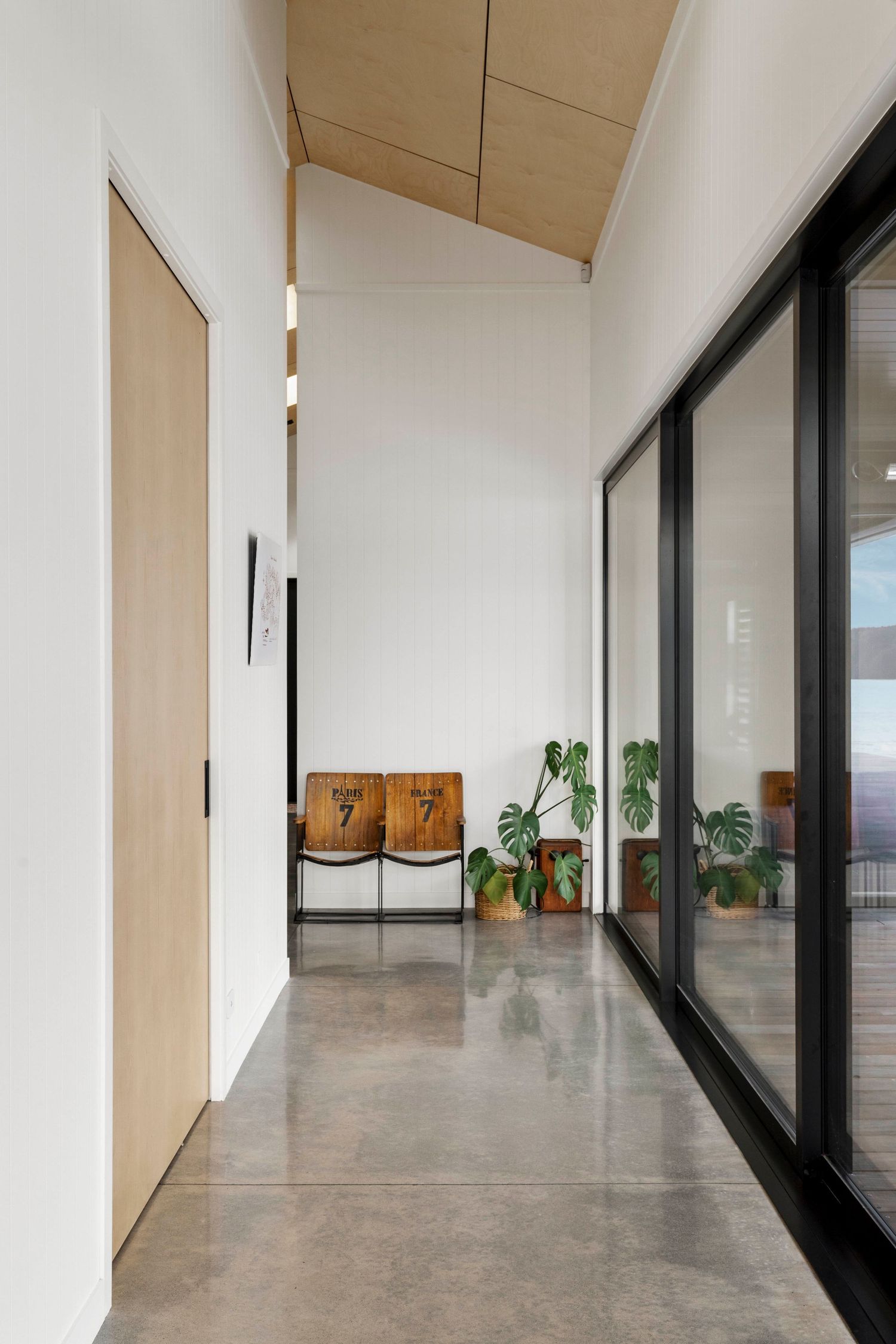 Modern minimalist hallway with white walls, concrete flooring, and large black-framed windows offering natural light.