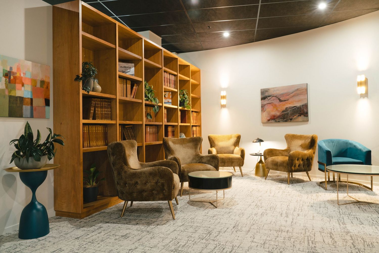 Modern lounge area with wooden bookshelf, plush seating, and contemporary decor in a cozy office or library setting.