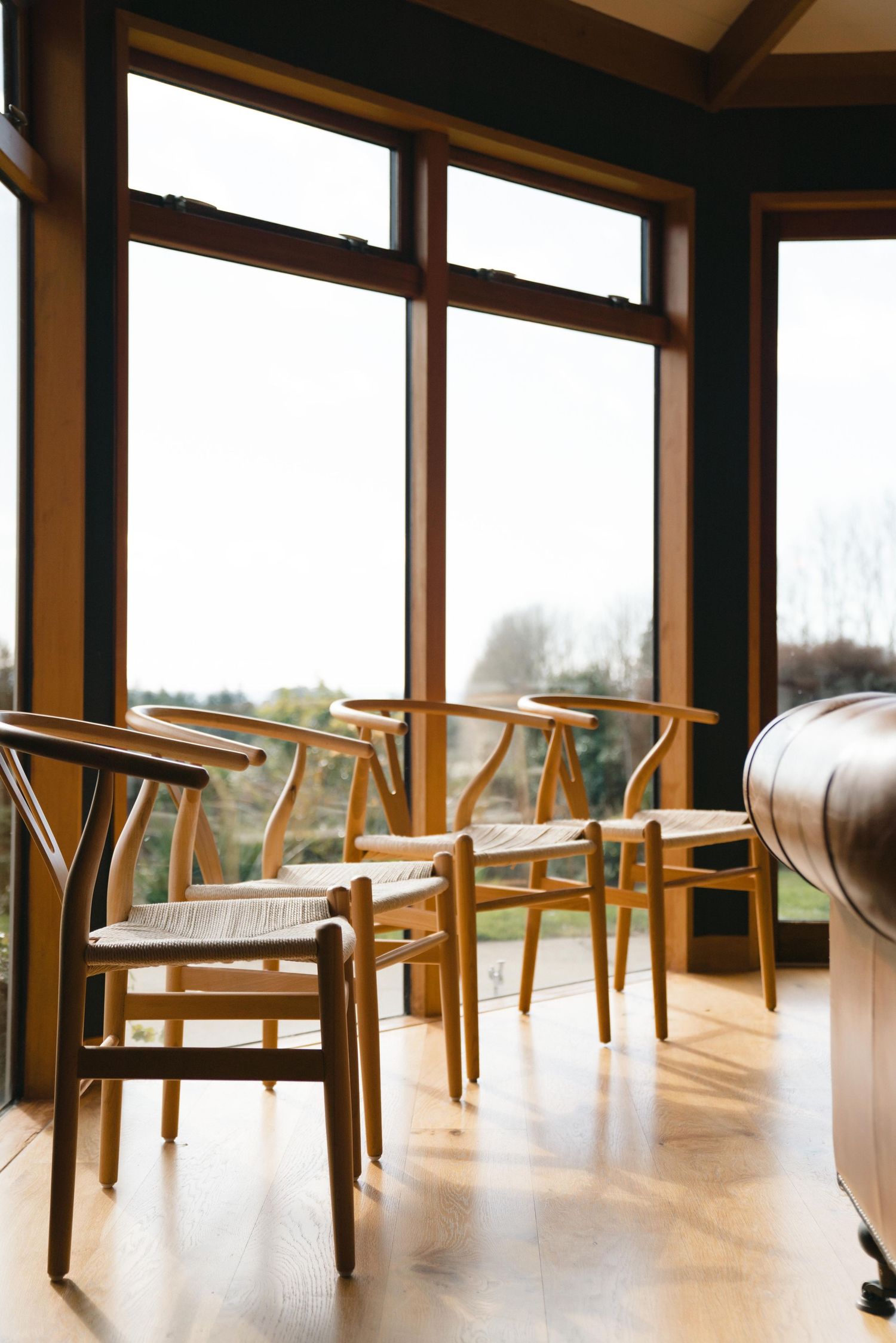 Wooden chairs arranged in front of large windows in a sunny room with hardwood floors.