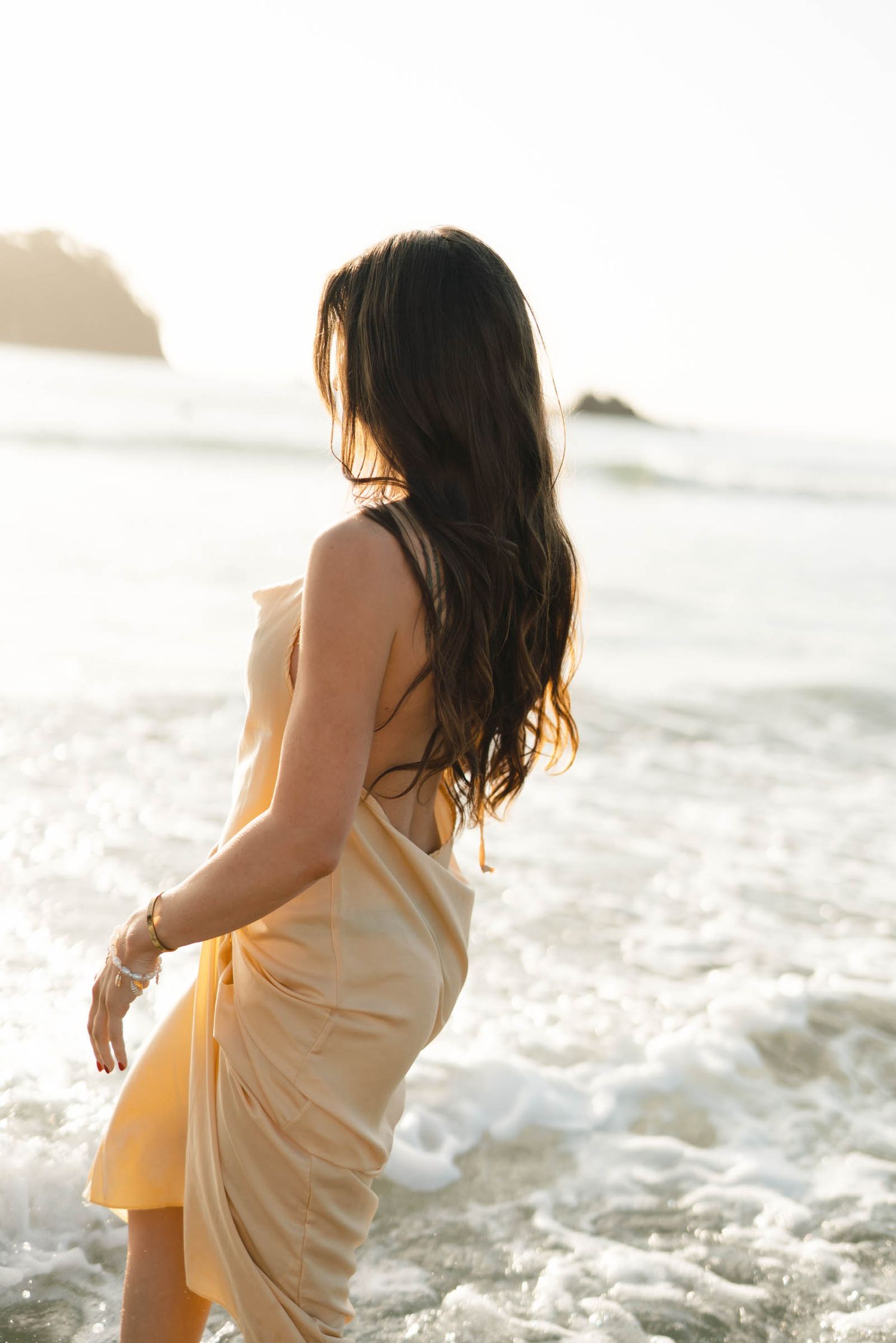 Person in a light dress dancing on a sunny beach with waves crashing behind them.