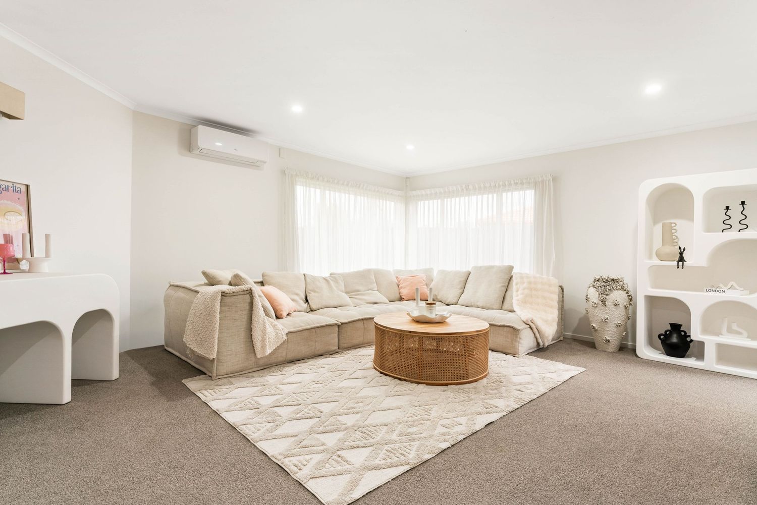 Bright modern living room with beige sectional sofa, round rattan coffee table and white arched wall niches.