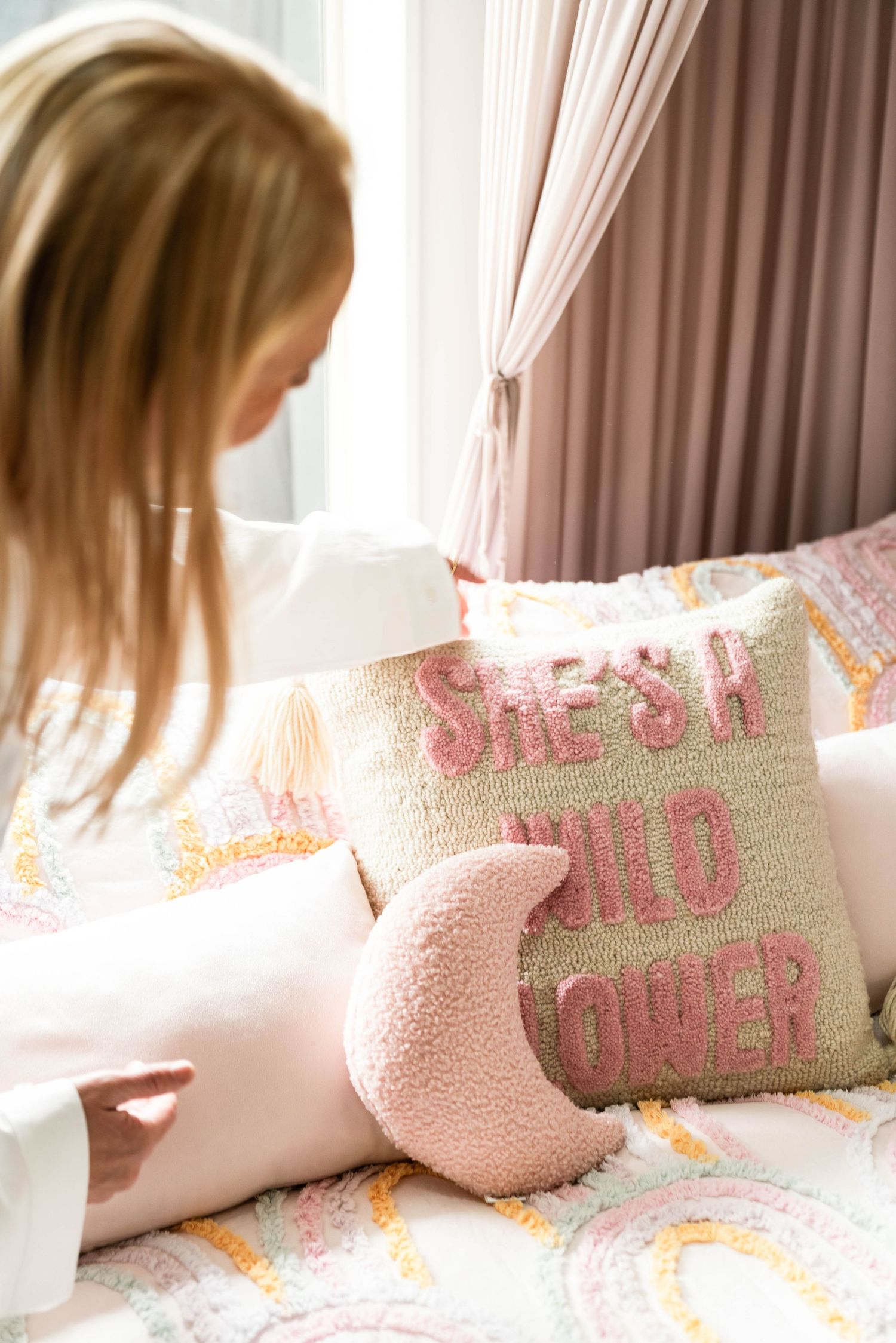 Pink and white decorative throw pillows with text on a cozy bed with curtains.