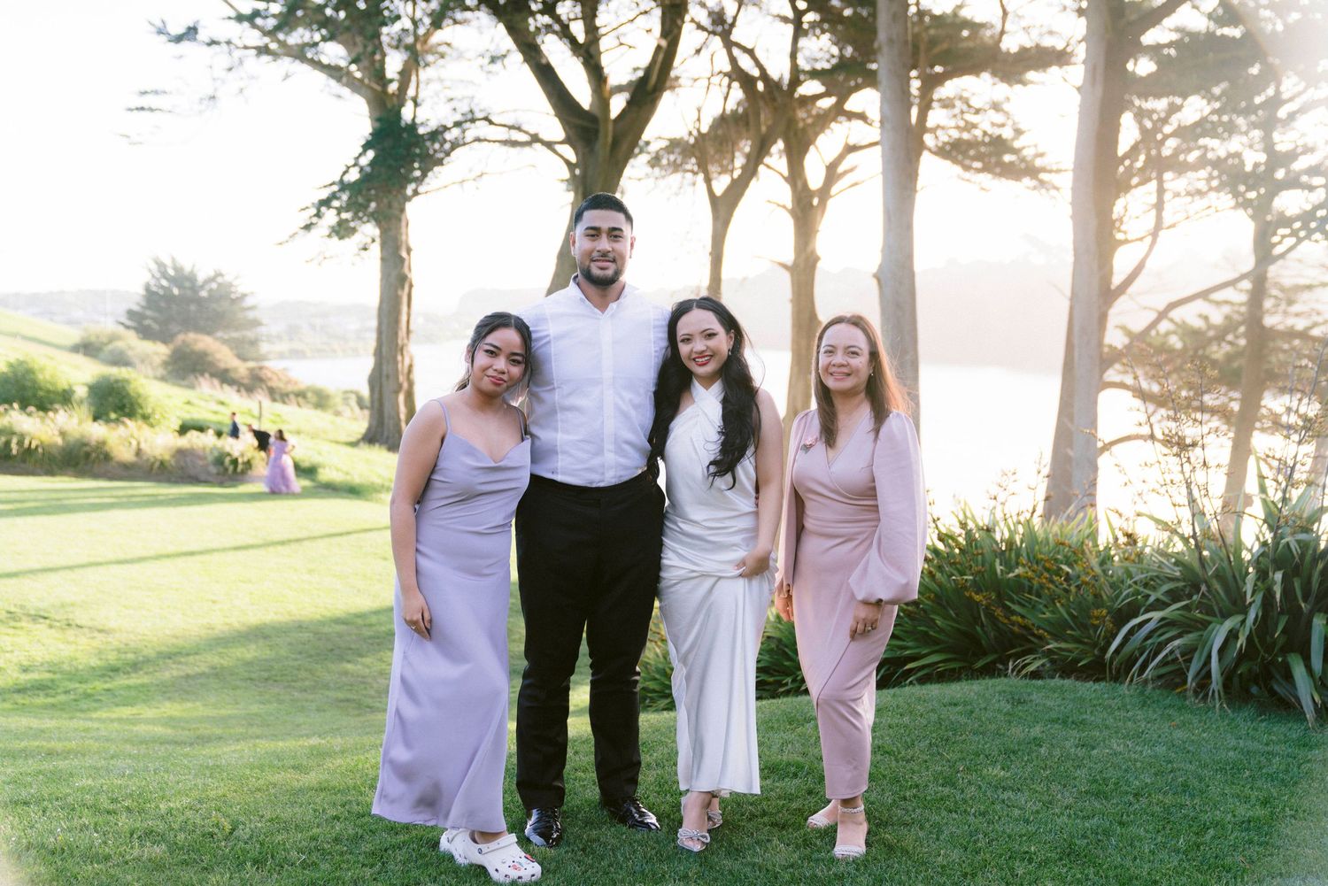 Wedding party poses together on a grassy hilltop with trees in the background during golden hour.