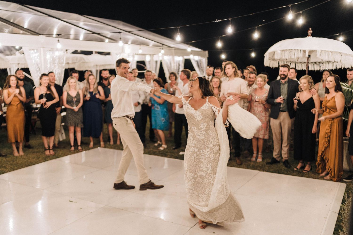 Wedding reception dance floor lit by string lights with guests dancing and celebrating.