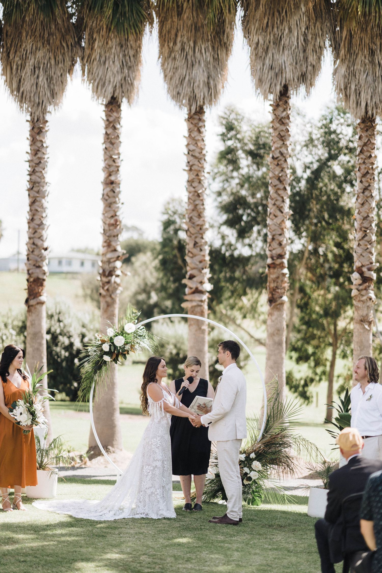 Outdoor wedding ceremony under towering palm trees as couple exchanges vows on a sunny afternoon.