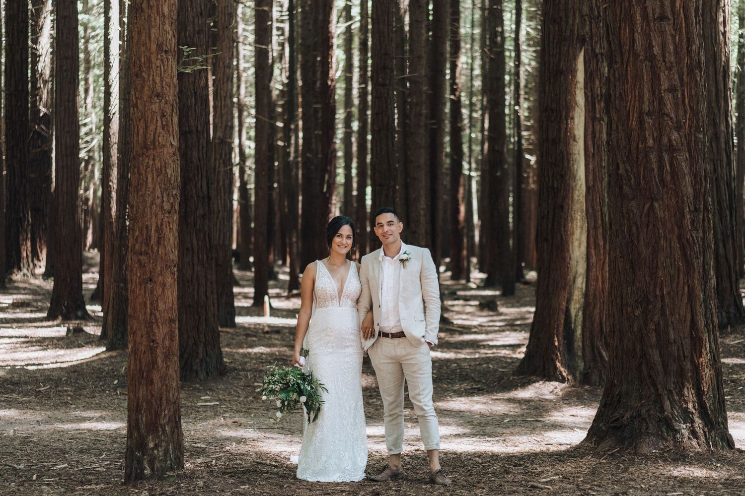 Wedding couple poses in a majestic redwood forest setting with tall trees creating natural columns.