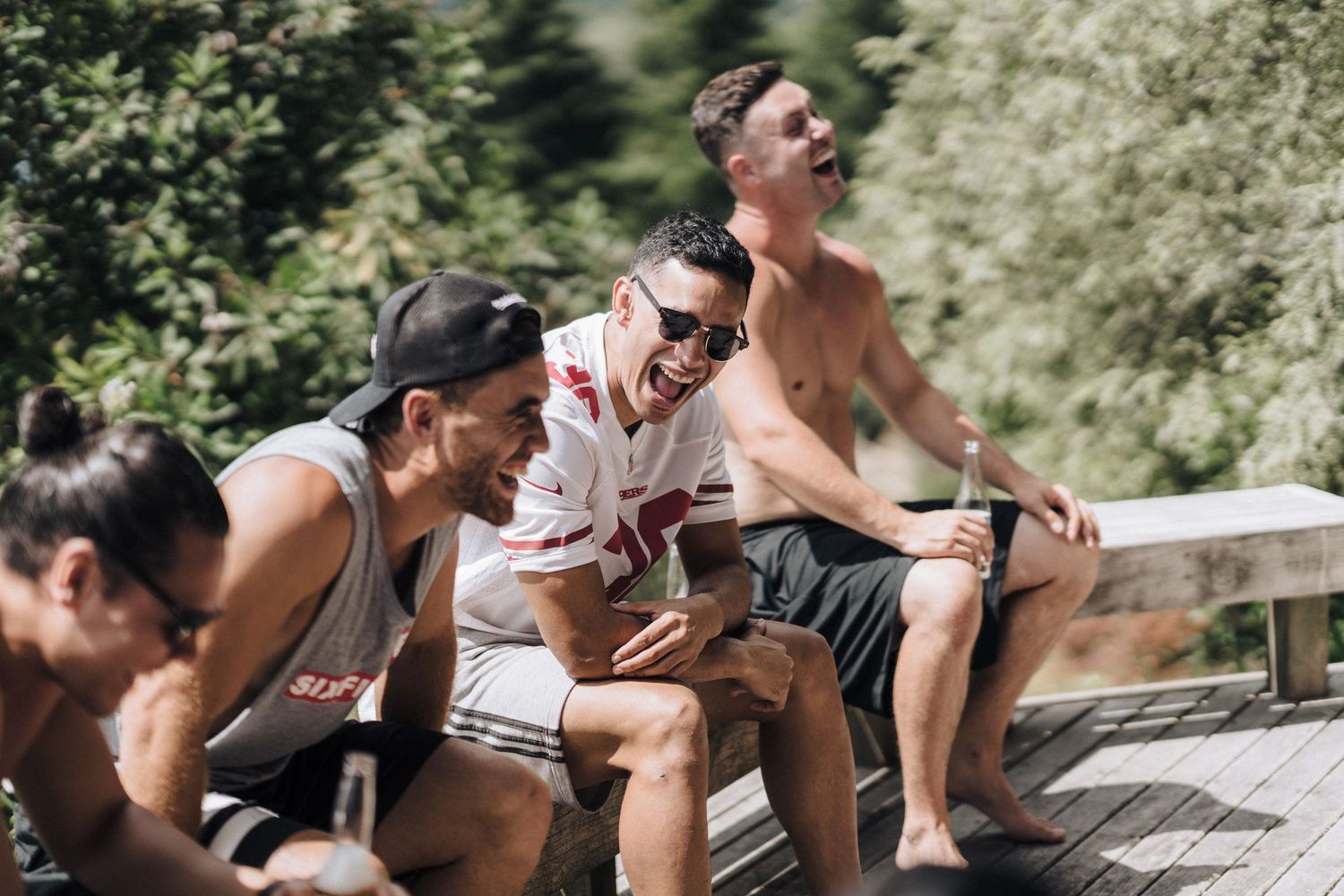 A group of friends laugh together while sitting outdoors on a sunny summer day.