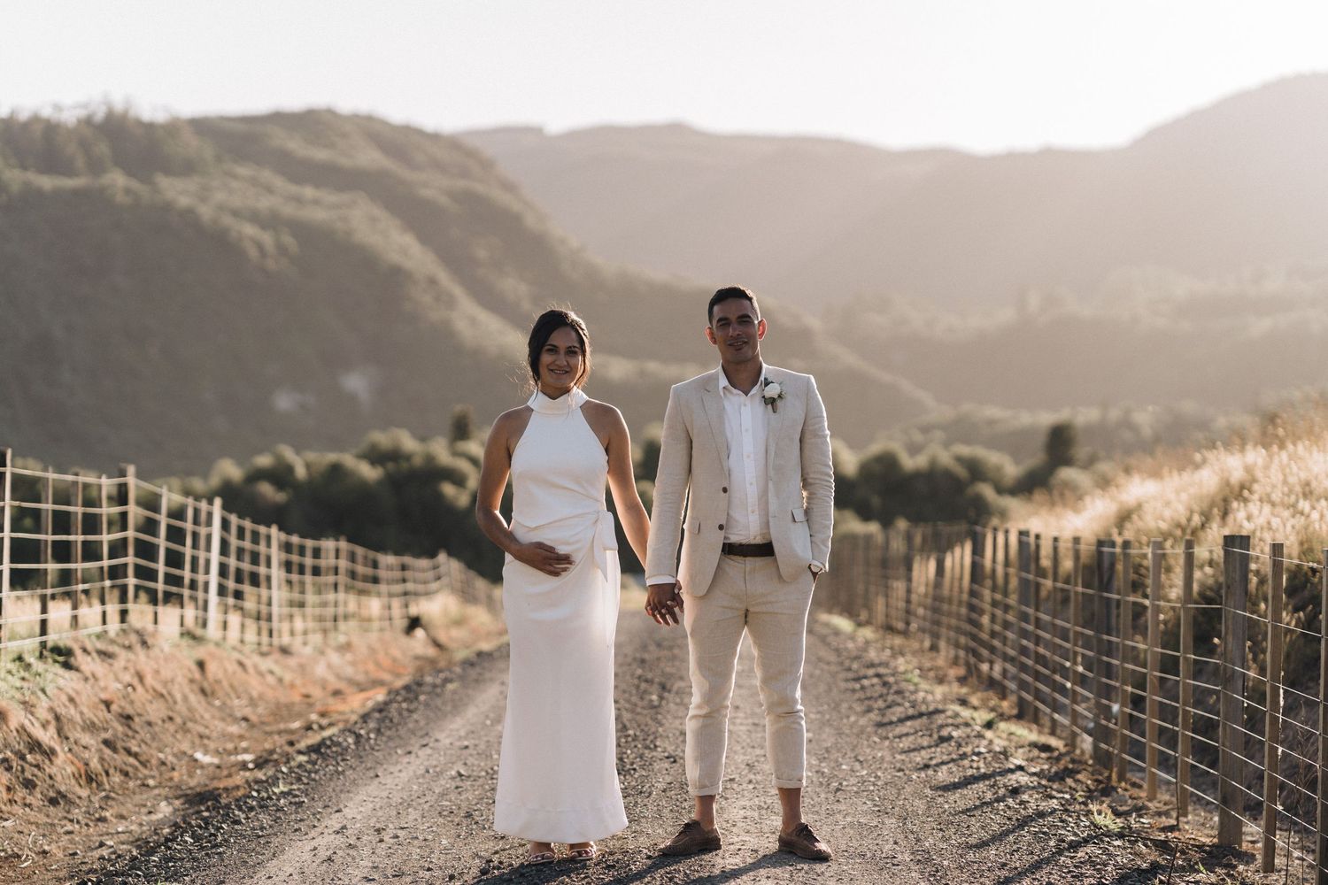 A couple poses on a dirt road with rolling hills in the background.