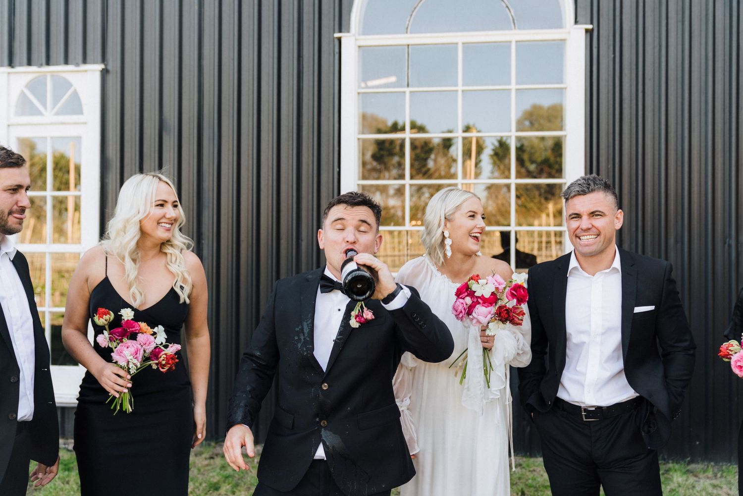 A celebratory moment with wedding party members in formal attire against a dark building exterior.