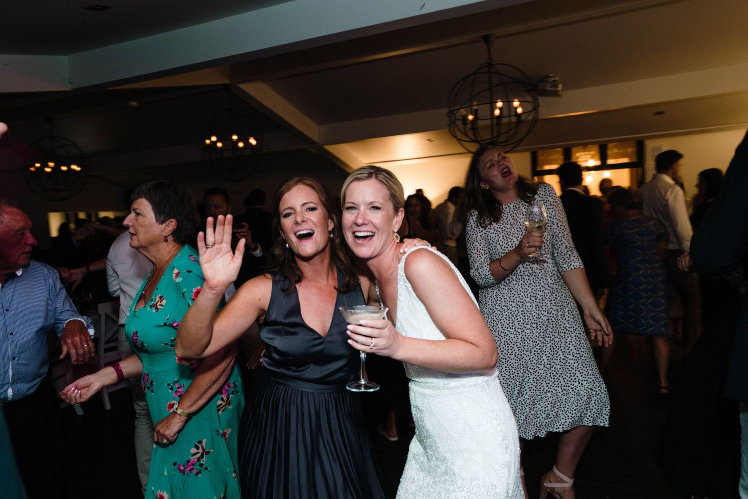 Wedding reception guests dancing and celebrating in a dimly lit indoor venue.