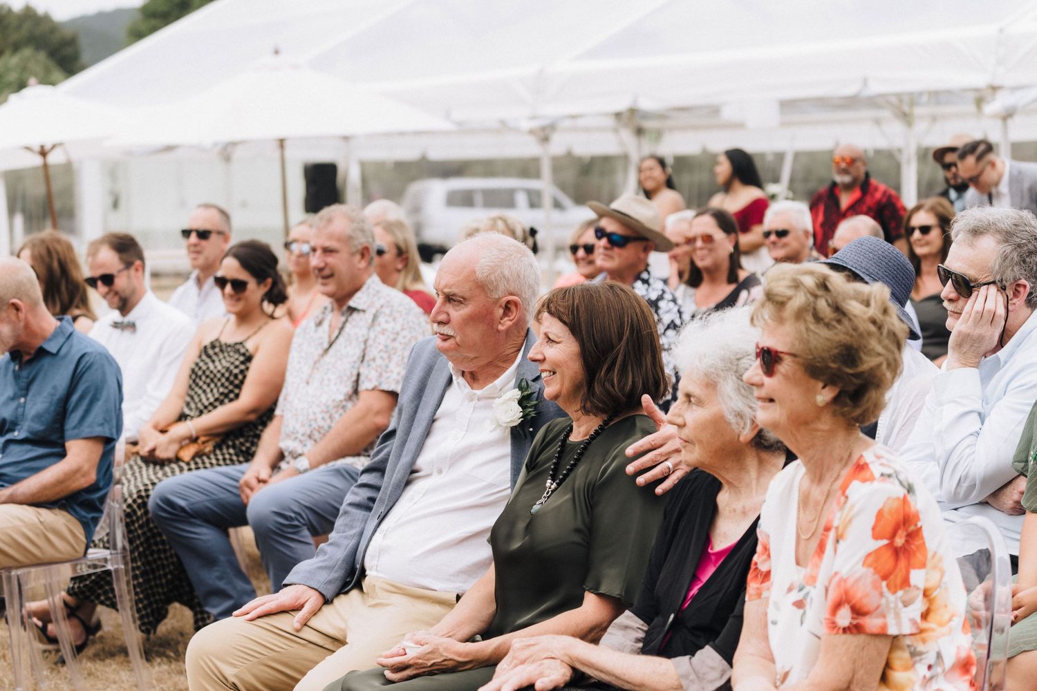 Wedding guests seated under white tent watching ceremony.