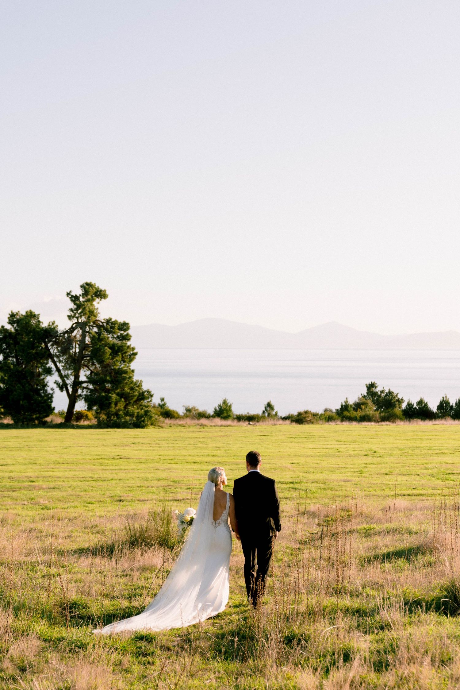 A couple walking through a serene meadow with mountains in the background on their wedding day.