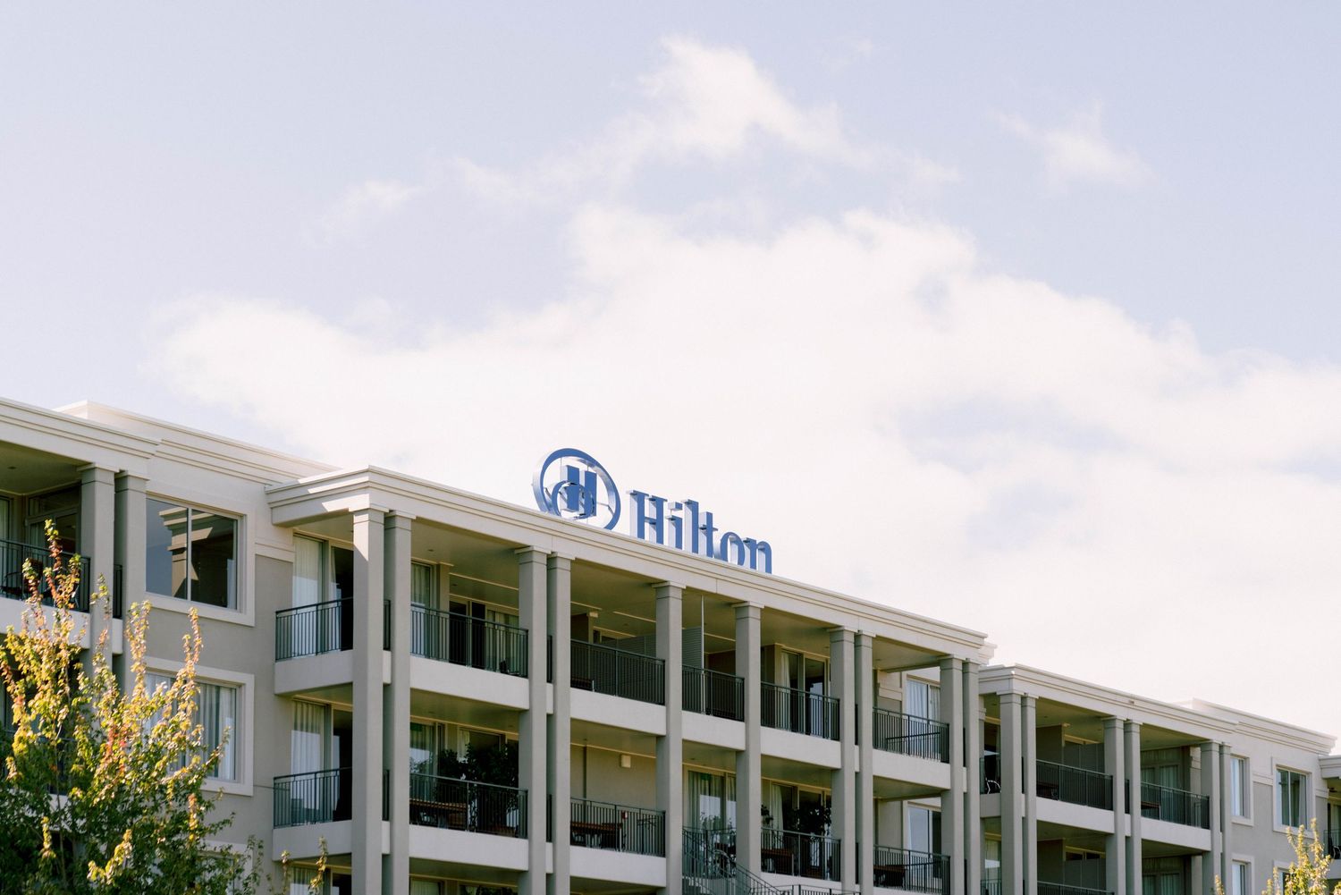 Hilton hotel building exterior with white facade and multiple floors against a blue cloudy sky.