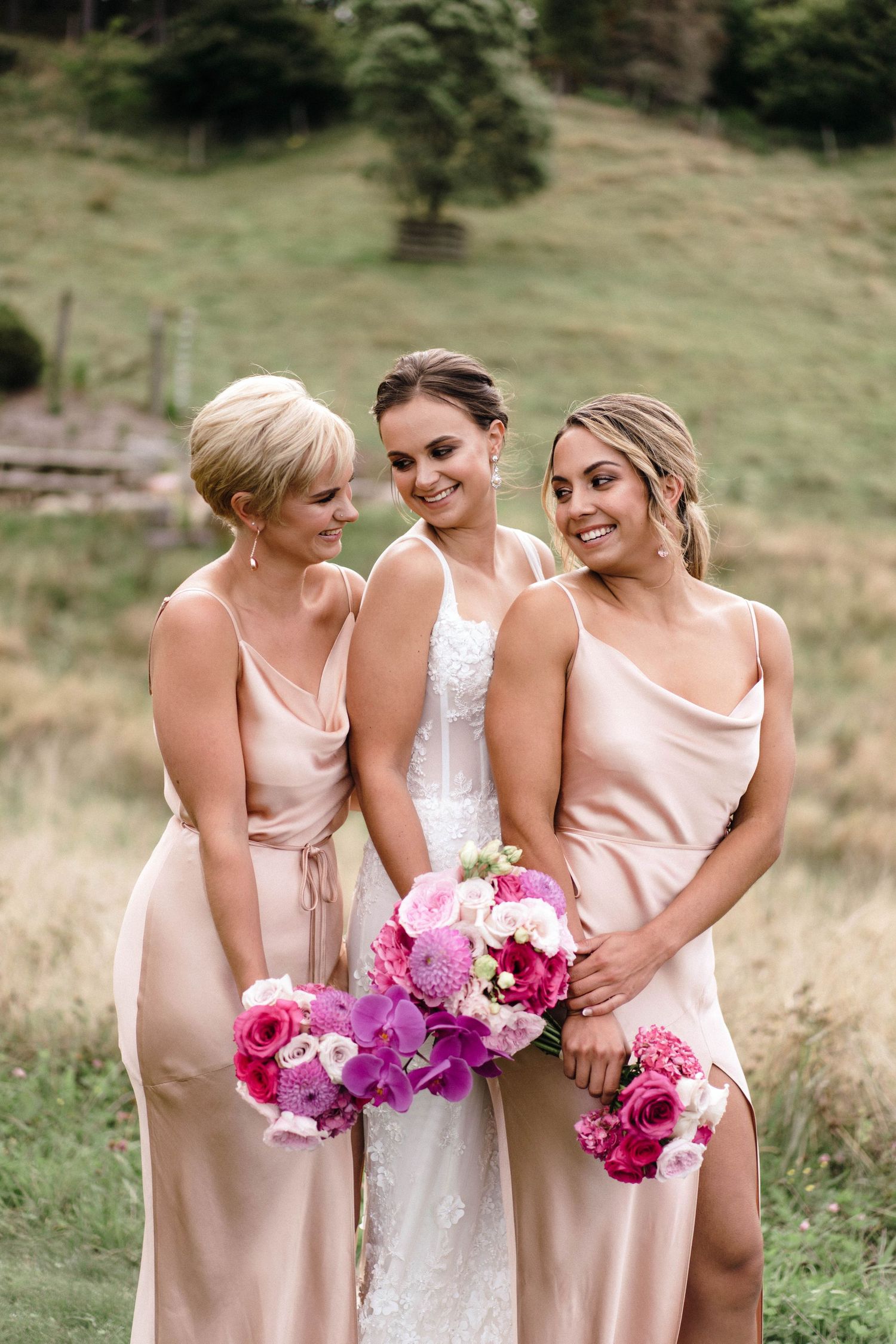 Bridesmaids in blush pink dresses holding vibrant pink and purple bouquets.