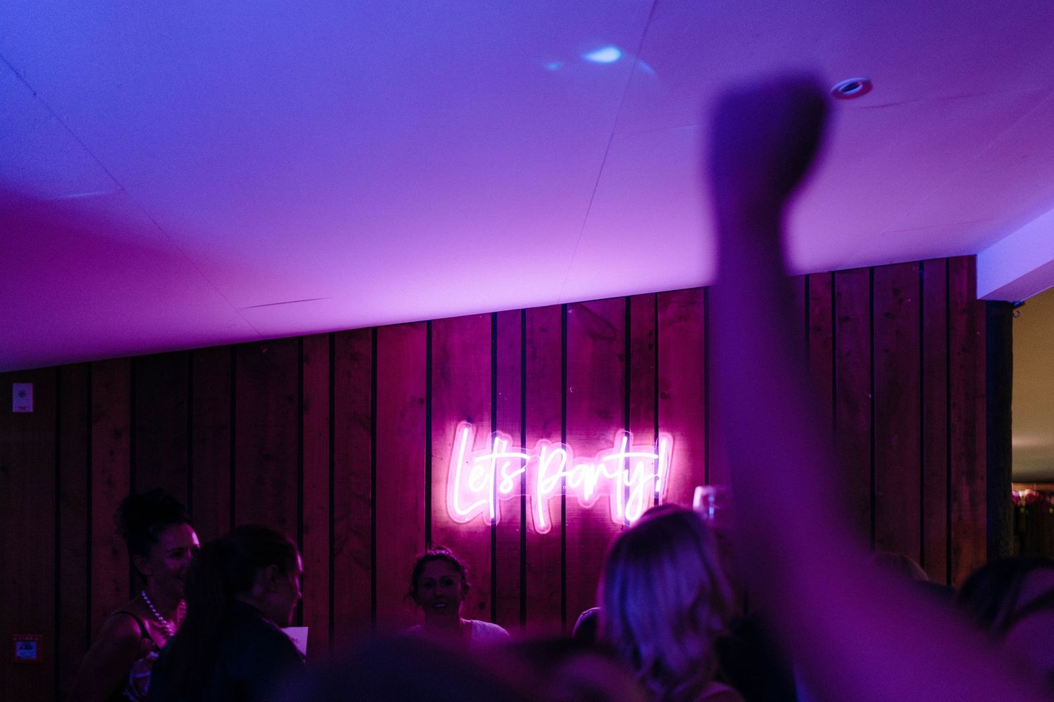 Purple mood lighting illuminating a wooden paneled wall at a wedding reception.