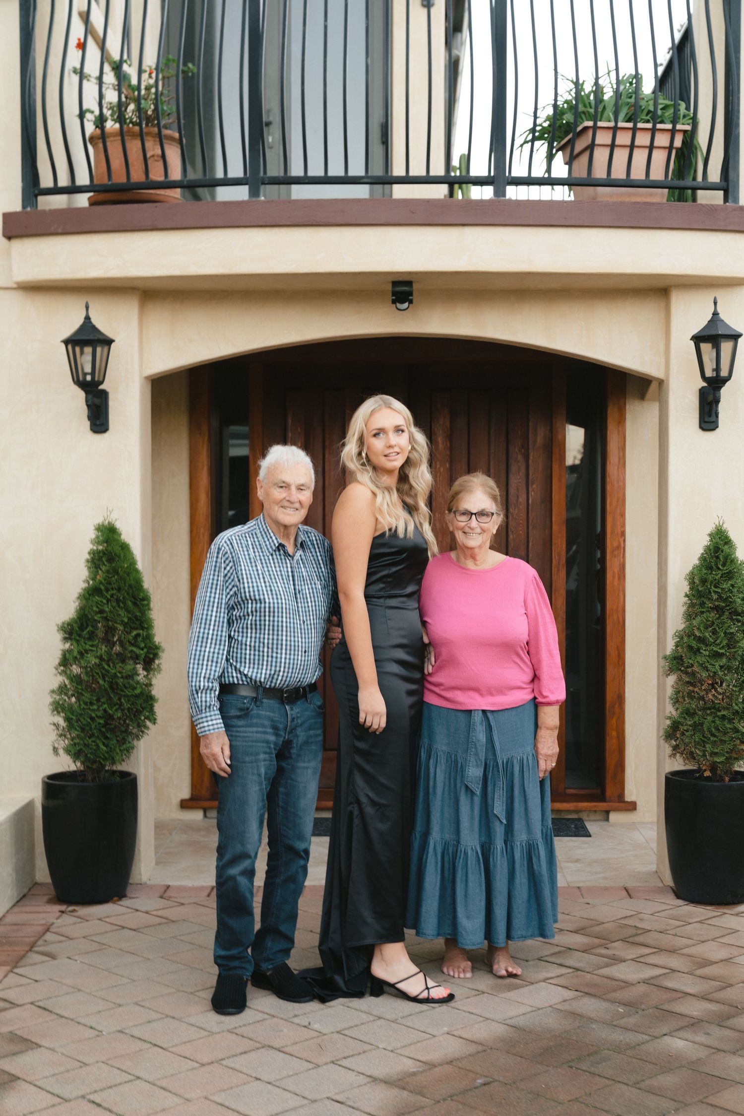 A family poses together outside an elegant entryway with lanterns and potted plants.