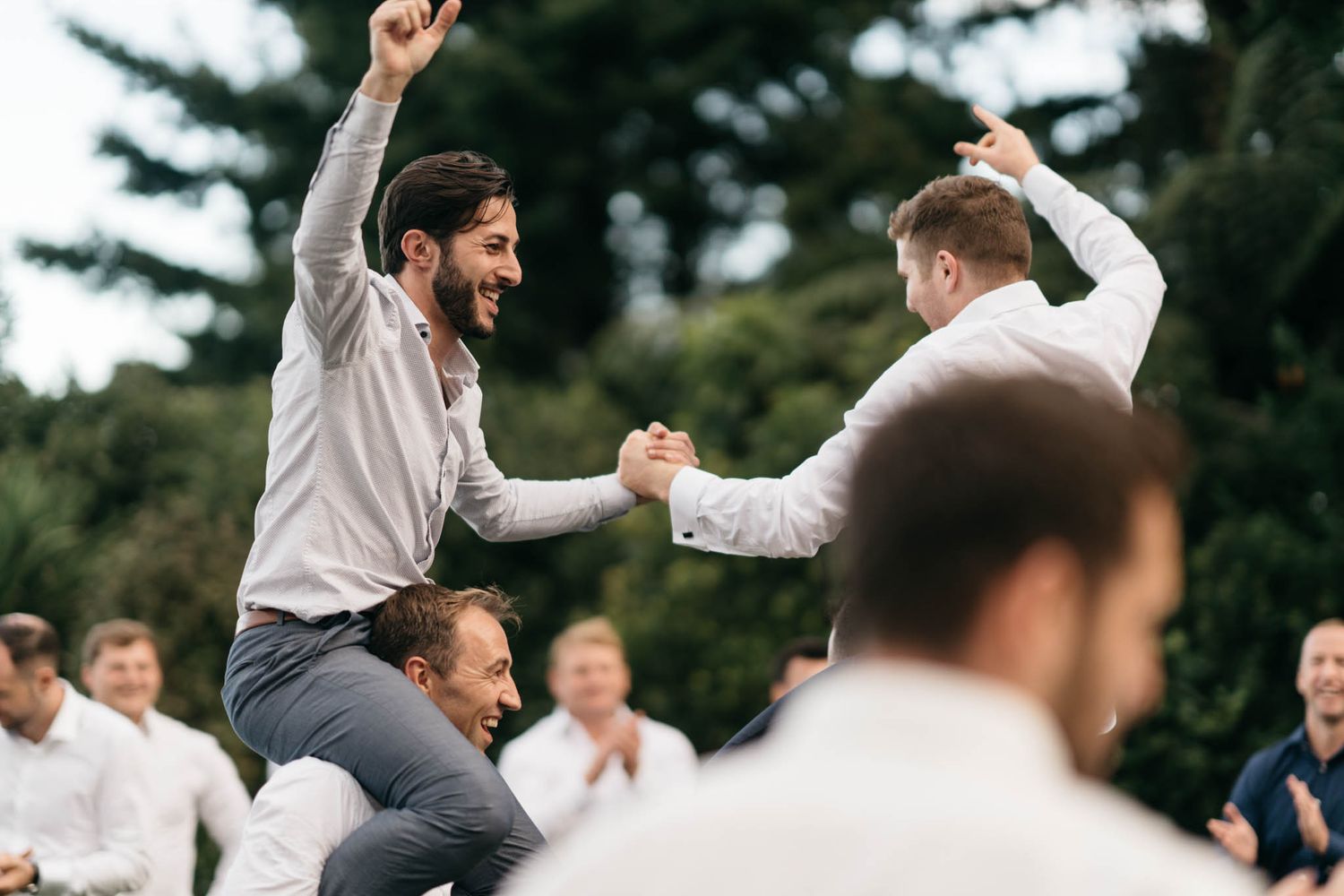 Two people celebrate joyfully at an outdoor celebration by dancing with their arms raised among a crowd.