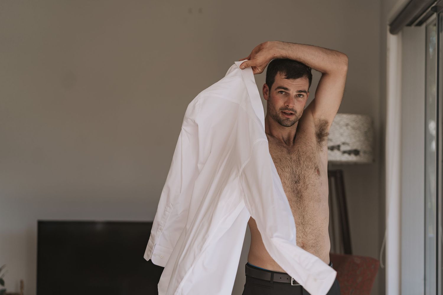Person with tousled hair wearing a white shirt stretches and moves expressively in an interior space.