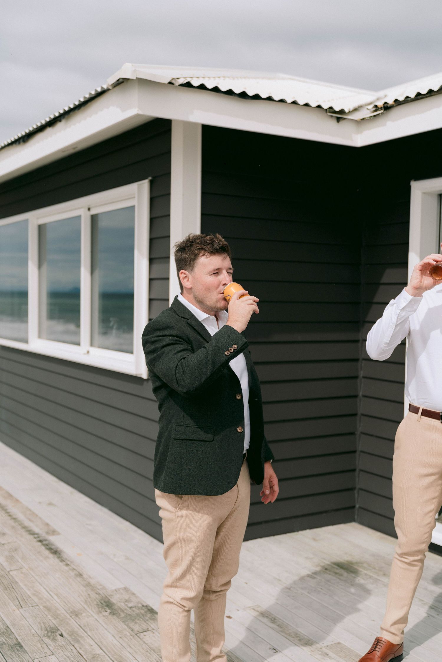 Two people in business casual attire drinking beverages outside a dark-sided building with windows.