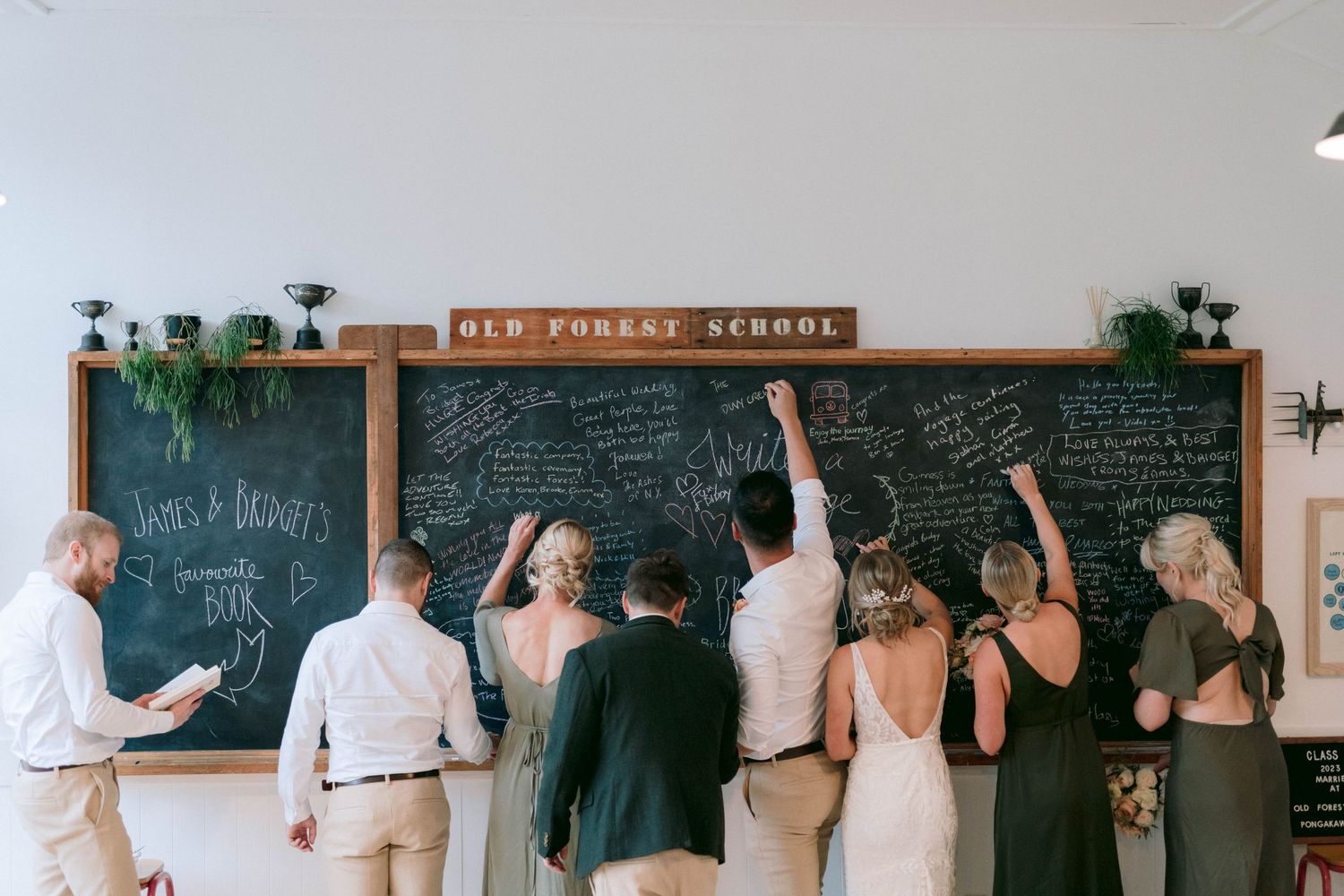 Wedding guests writing messages on chalkboard wall during reception celebration.