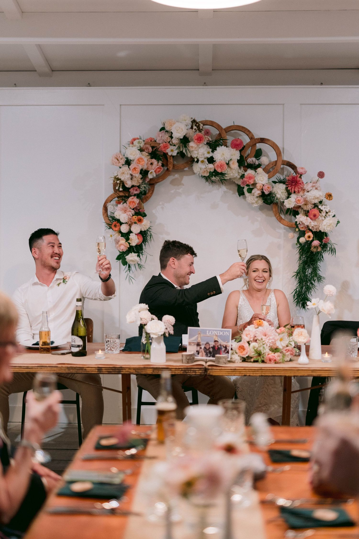 Wedding celebration with couple sitting at rustic table under floral arch decorated with pink and white roses.