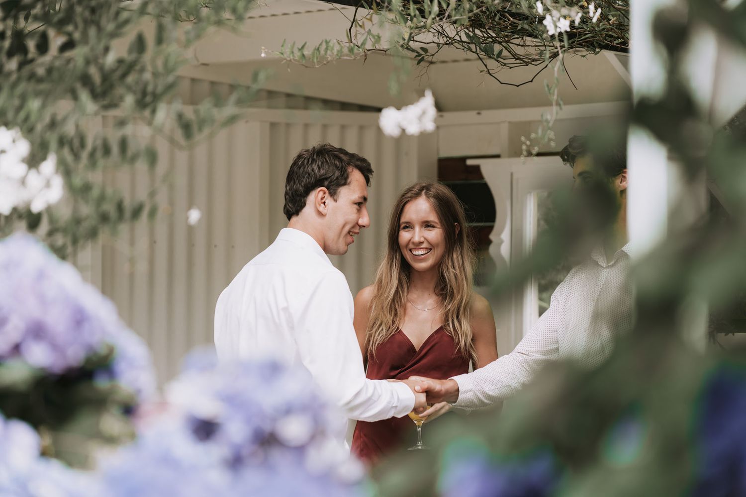 A couple shares a joyful moment together on a porch surrounded by purple hydrangeas and greenery.