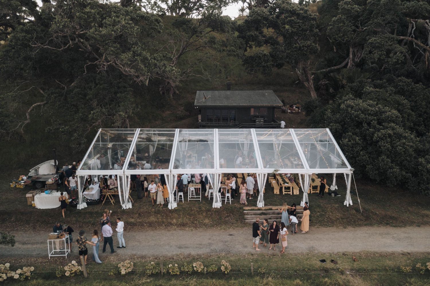 Panoramic view of an outdoor wedding pergola and seating arrangement framed by lush trees in a natural setting.