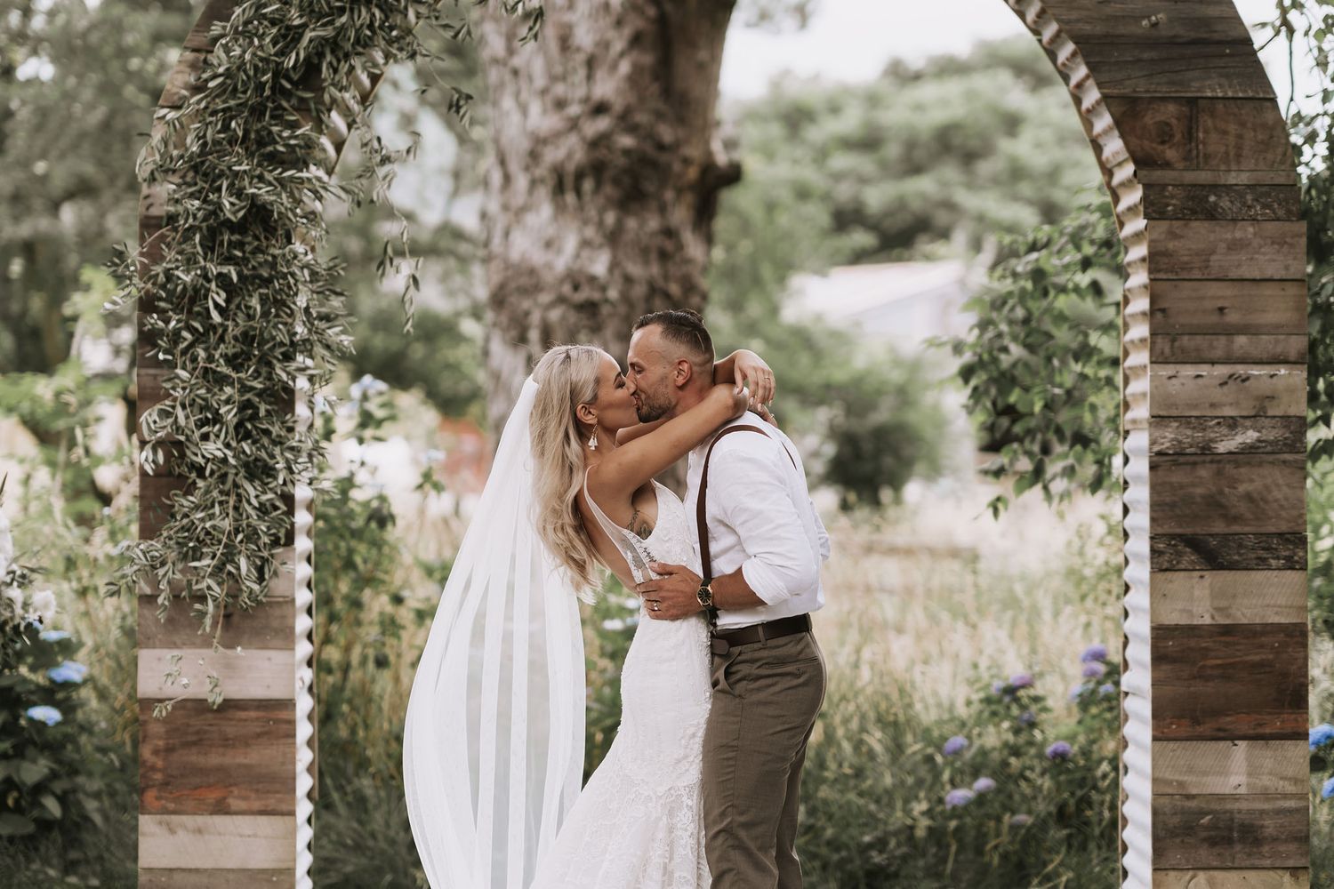 Romantic garden wedding ceremony with wooden arches and black iron gates covered in floral arrangements and greenery.