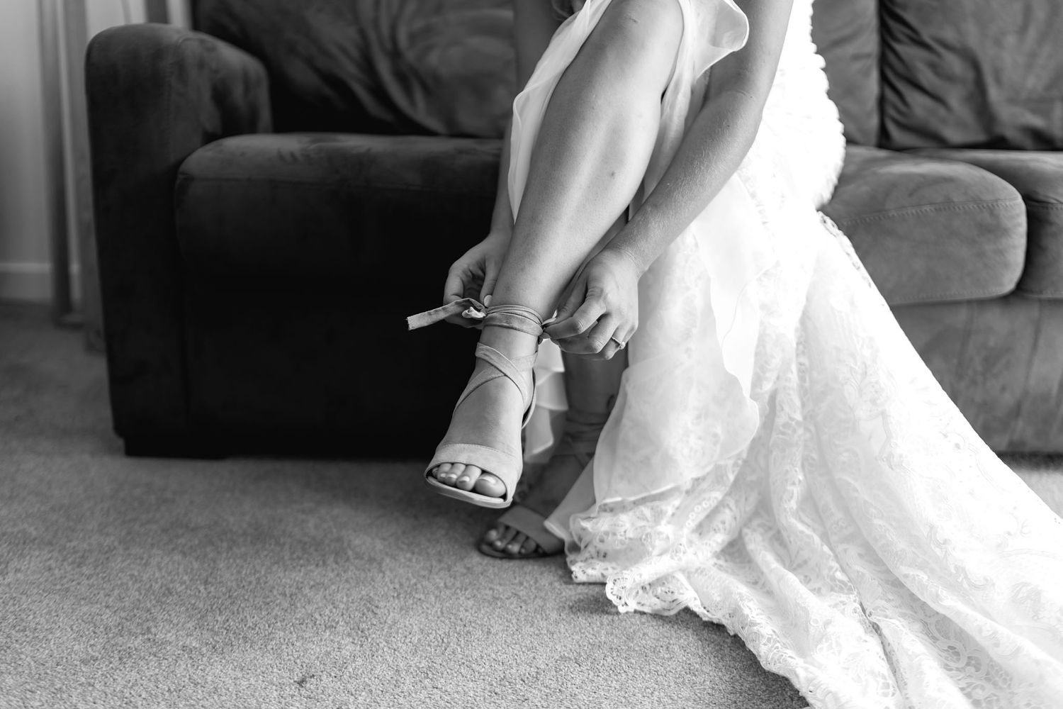 Close-up shot of bridal shoes and wedding dress hem details in black and white.