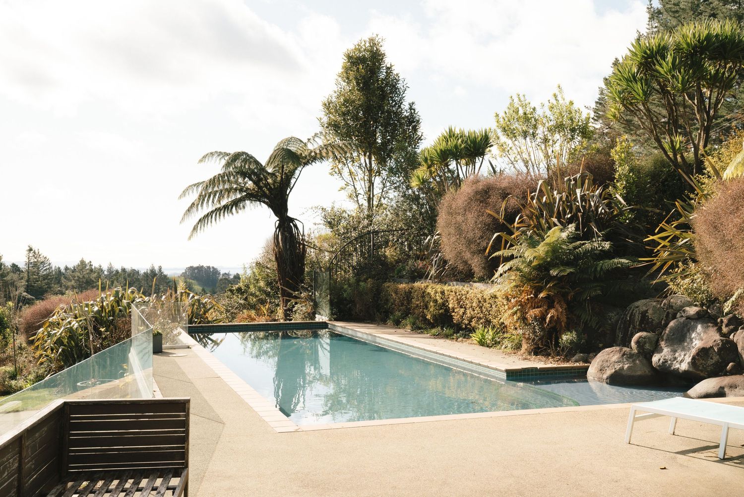 Modern swimming pool surrounded by tropical landscaping and palm trees on a sundeck with a mountain view backdrop.