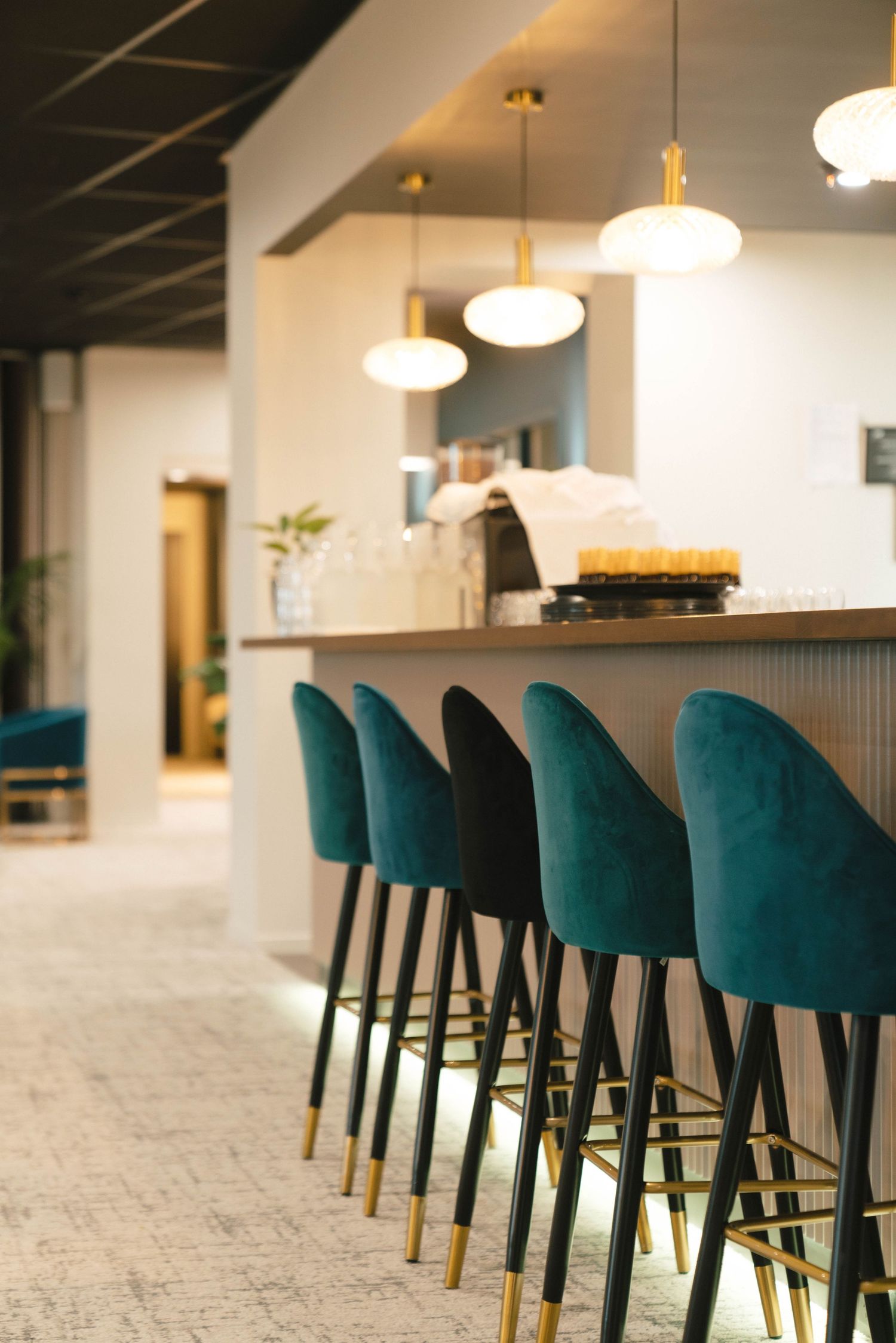 Modern bar area with emerald green velvet barstools and pendant lights in a stylish interior space.