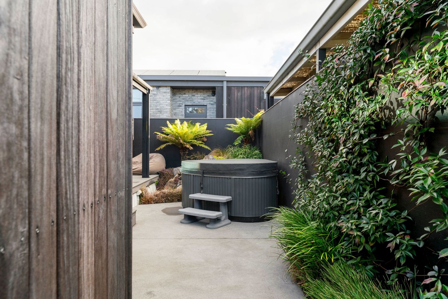 Modern outdoor patio space with hot tub, lush greenery and wooden privacy fence in an urban setting.