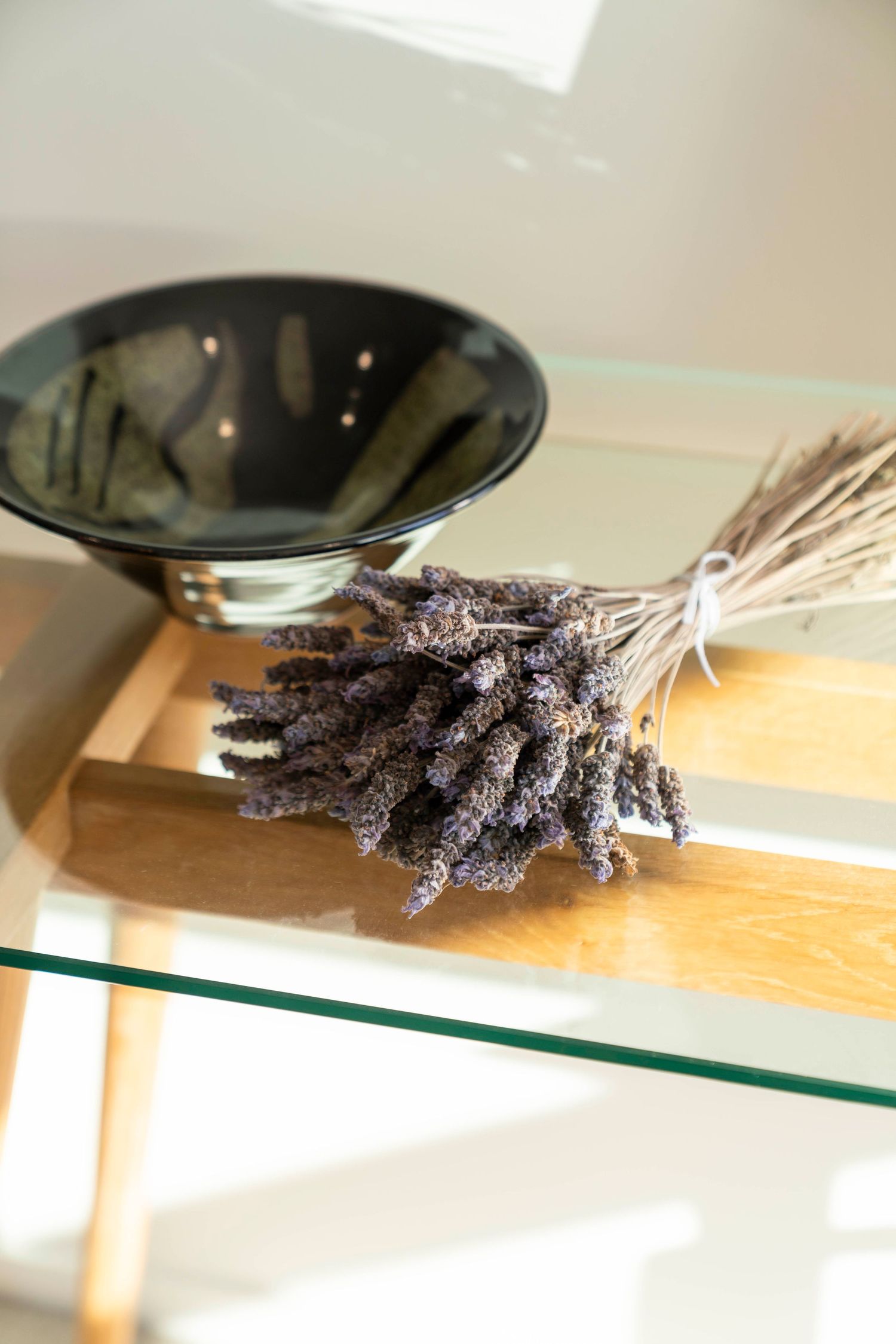 Dried lavender bundles laying together on a wooden surface create natural shadows against a glass shelf backdrop.