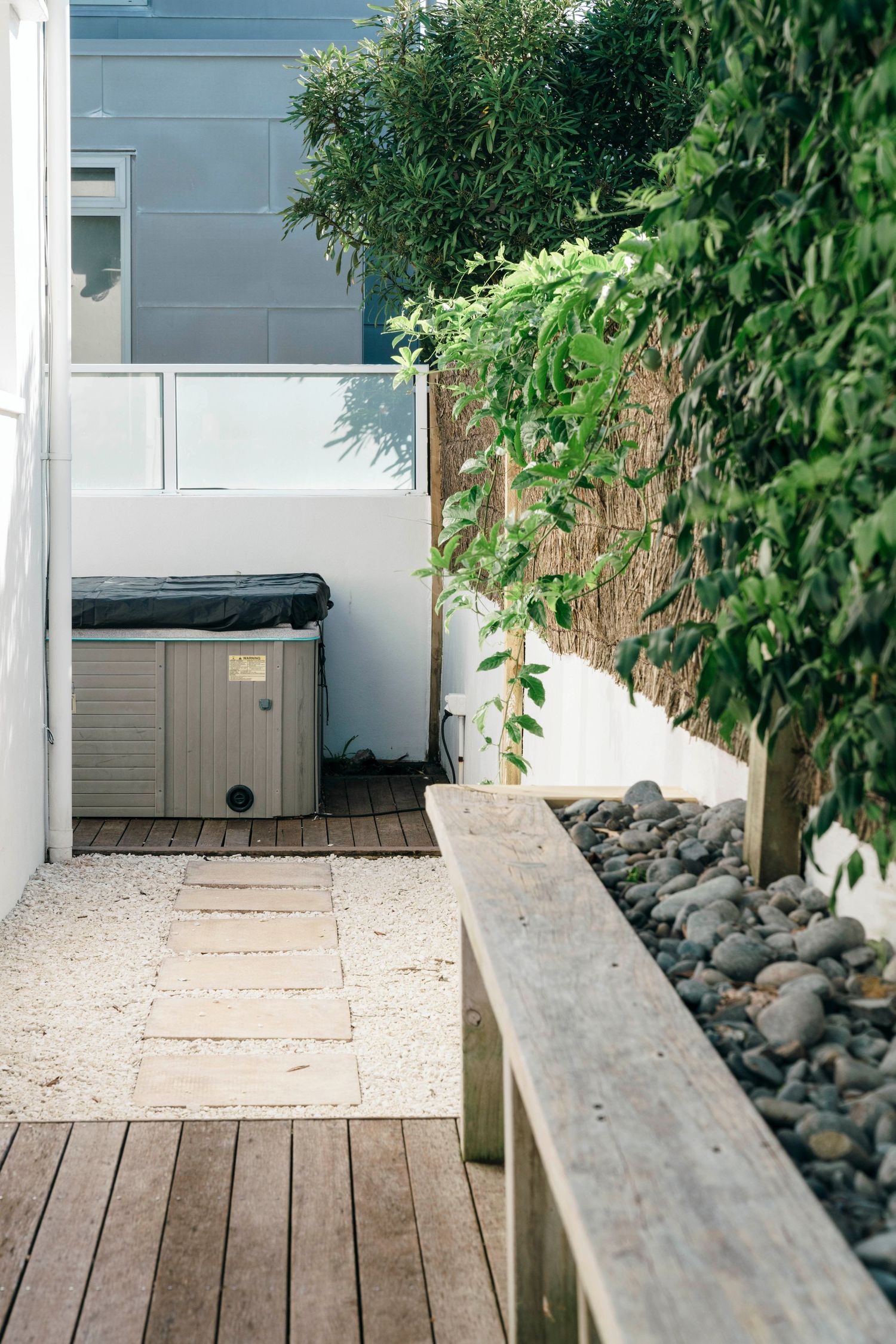 Modern backyard patio space with wooden deck, white gravel, and hot tub installation.