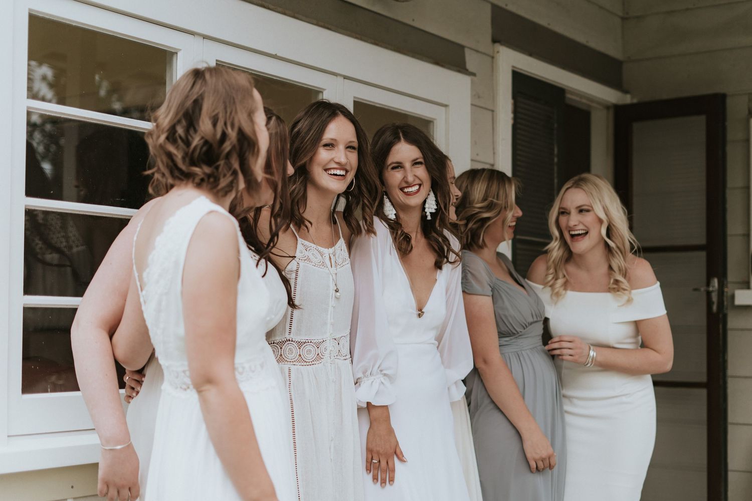 A group of bridesmaids in white dresses stand together laughing and having fun at a wedding celebration.