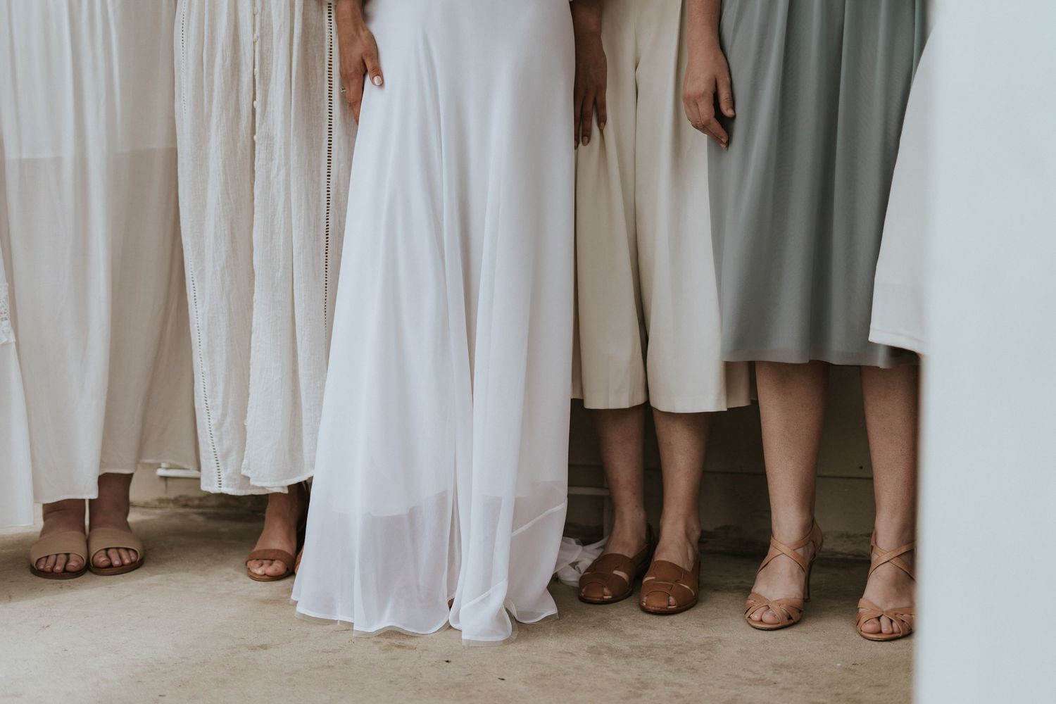 A row of people standing together wearing light colored dresses and formal attire showing their shoes and hemlines.