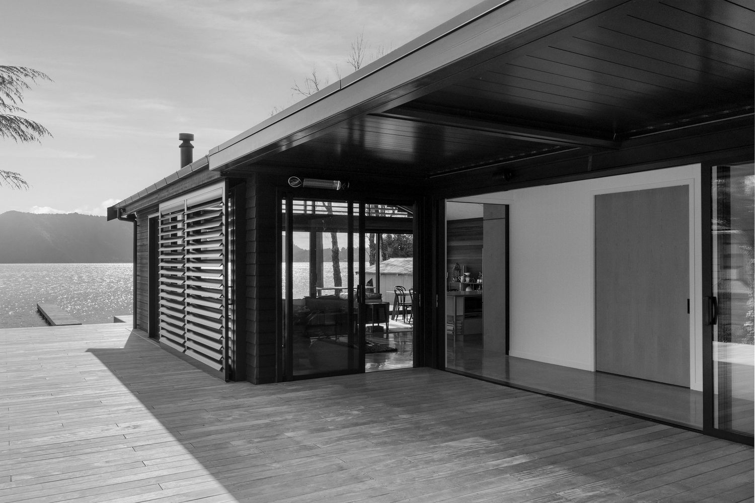 Modern lakeside home with covered deck and sliding glass doors features contemporary wooden slat design in black and white.