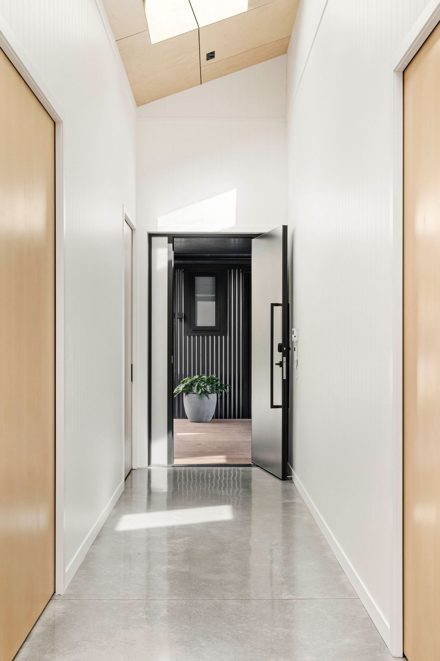 Modern minimalist office hallway with white walls, beige accents, and reflective flooring illuminated by natural light.